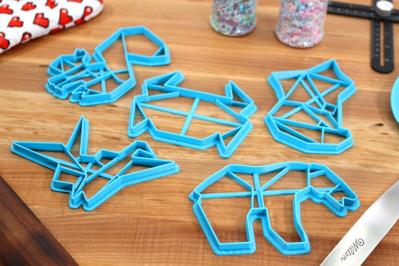 May include: Five blue plastic cookie cutters shaped like origami animals. The cutters are on a wooden surface.