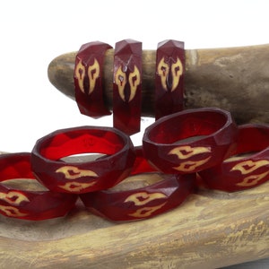 May include: A set of eight red resin rings with a geometric design and a yellow flame pattern. The rings are stacked on a wooden surface.