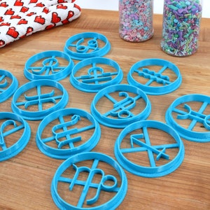 May include: A set of twelve blue plastic cookie cutters shaped like the astrological signs. The cutters are arranged on a wooden surface.