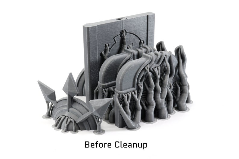 May include: A 3D printed model of a fantasy creature with multiple arms and a large, flat head. The creature is standing on a base with a textured surface. The model is gray and has a rough, unfinished appearance. Before Cleanup.