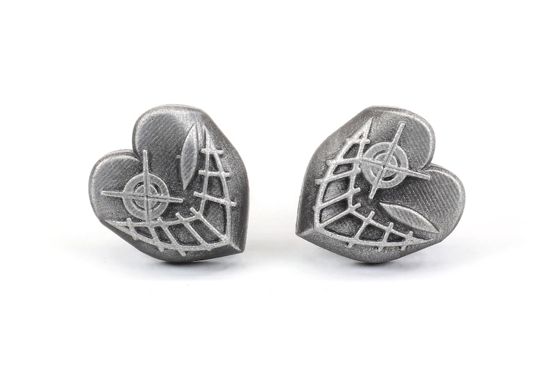 May include: A pair of silver heart-shaped earrings with a detailed design of a web and a crosshair.