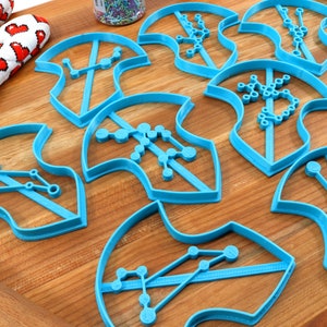 Puede incluir: Un conjunto de nueve cortadores de galletas de pl&aacute;stico azul con forma de hojas con diferentes dise&ntilde;os de constelaciones en su interior.