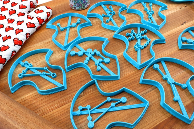 Puede incluir: Un conjunto de nueve cortadores de galletas de pl&aacute;stico azul con forma de hojas con diferentes dise&ntilde;os de constelaciones en su interior.