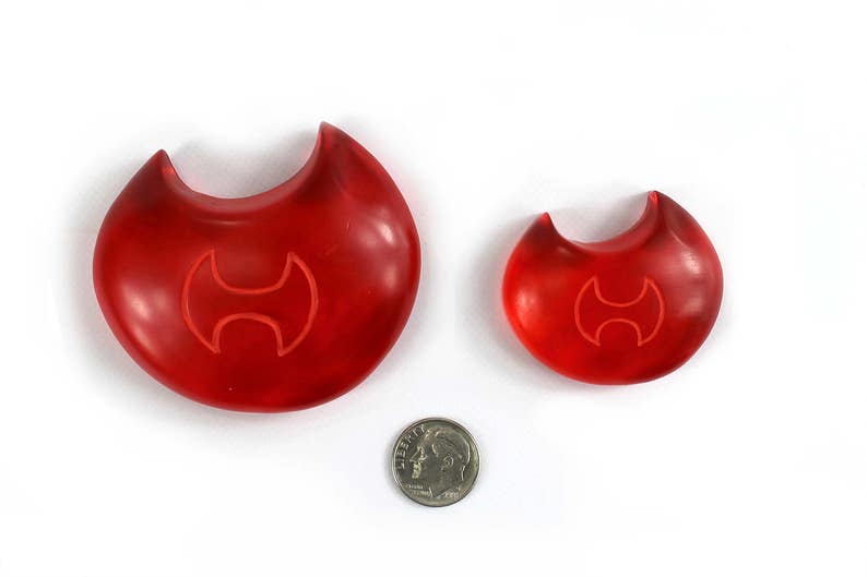 May include: Two red plastic musical instruments shaped like a crescent moon with a stylized axe symbol in the center. The larger instrument is about 4 inches in diameter and the smaller instrument is about 2 inches in diameter.