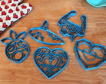 Puede incluir: Seis cortadores de galletas de plástico azul con forma de corazón, corazón con diseño, objeto de videojuego, objeto de videojuego, objeto de videojuego y objeto de videojuego.