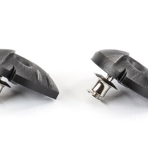 May include: Two black plastic shoe cleats with a silver metal pin. The cleats have a textured surface and are designed to provide traction on slippery surfaces.