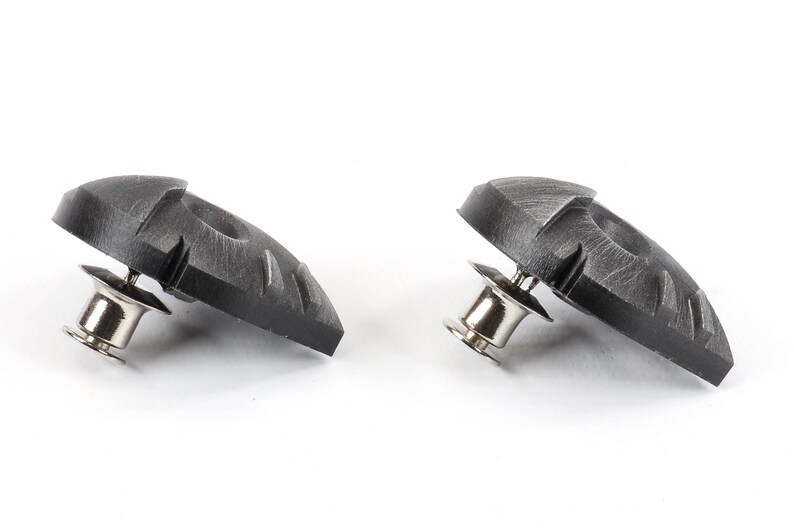 May include: Two black plastic shoe cleats with a silver metal pin. The cleats have a textured surface and are designed to provide traction on slippery surfaces.