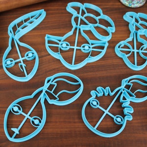 May include: A set of six blue plastic cookie cutters shaped like different characters from the Star Wars franchise. The cutters are on a wooden surface.