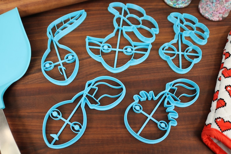 May include: A set of six blue plastic cookie cutters shaped like different characters from the Star Wars franchise. The cutters are on a wooden surface.