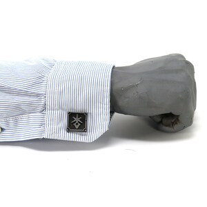 May include: A close-up of a blue and white striped dress shirt cuff with a silver cufflink featuring a geometric design.
