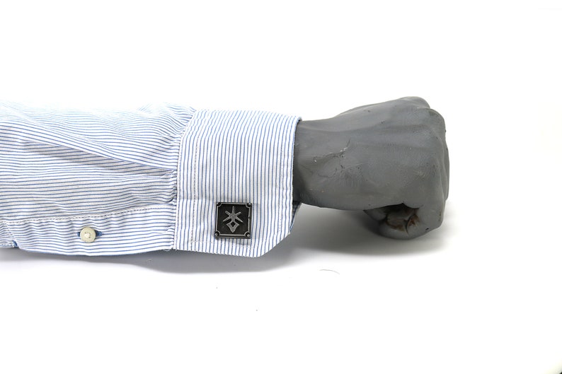 May include: A close-up of a blue and white striped dress shirt cuff with a silver cufflink featuring a geometric design.