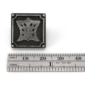 May include: A silver metal square decorative accent with a cutout design of a stylized floral motif. The accent is approximately 2 cm wide.