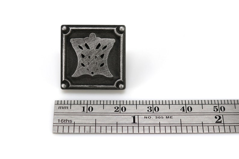 May include: A silver metal square decorative accent with a cutout design of a stylized floral motif. The accent is approximately 2 cm wide.