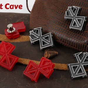 May include: Four metal and plastic pins with a geometric design. The pins are in the shape of a cross with a point at the top. Two of the pins are silver and two are red. The pins are on a brown leather surface. The text "Loot Cave" is visible in the top left corner of the image.