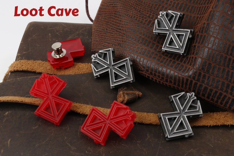 May include: Four metal and plastic pins with a geometric design. The pins are in the shape of a cross with a point at the top. Two of the pins are silver and two are red. The pins are on a brown leather surface. The text "Loot Cave" is visible in the top left corner of the image.