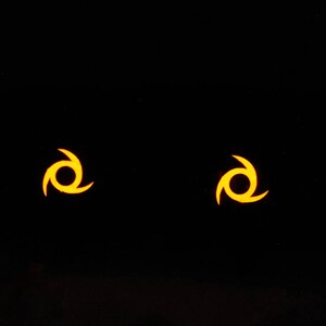 May include: Two yellow stylized symbols on a black background. Each symbol is a three-pointed star with a circle in the center.