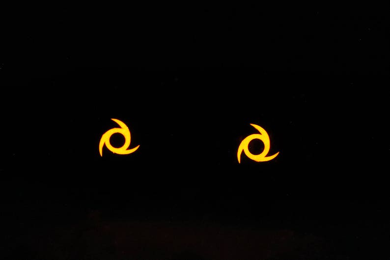 May include: Two yellow stylized symbols on a black background. Each symbol is a three-pointed star with a circle in the center.