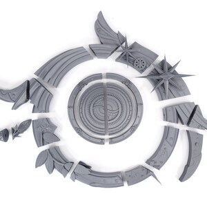 May include: A gray, disassembled decorative object with a circular central design and various stylized elements. The pieces include star shapes, leaf motifs, and curved segments, all arranged on a white background.