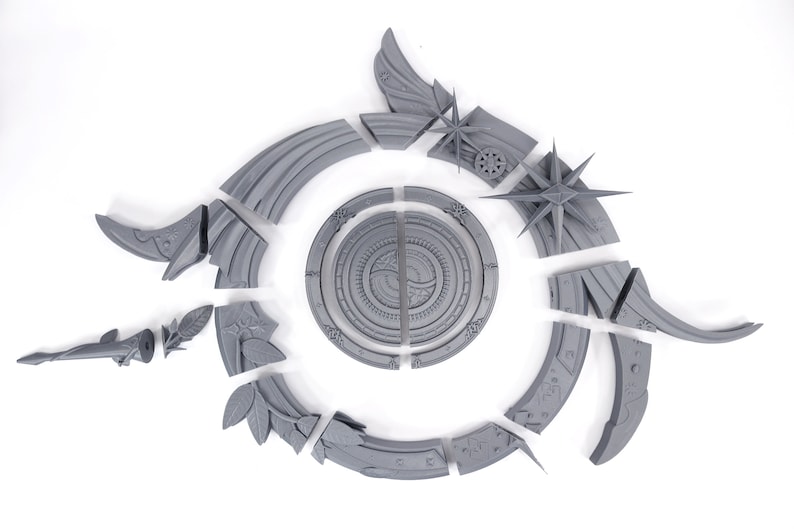 May include: A gray, disassembled decorative object with a circular central design and various stylized elements. The pieces include star shapes, leaf motifs, and curved segments, all arranged on a white background.