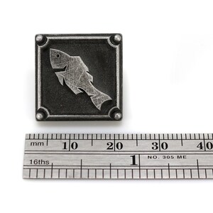 May include: A silver metal square with a stylized fish design. The square is about 2 cm wide.