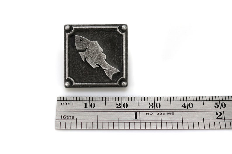 May include: A silver metal square with a stylized fish design. The square is about 2 cm wide.