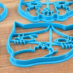 May include: A set of four blue plastic cookie cutters shaped like animal faces. The cutters are on a wooden surface.
