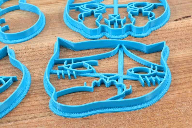 May include: A set of four blue plastic cookie cutters shaped like animal faces. The cutters are on a wooden surface.