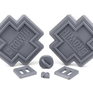 May include: A set of gray plastic building blocks with the word "GROWTH" embossed on two of the blocks. The blocks are shaped like a cross and have a variety of other shapes, including a circle, a square, and a rectangle.