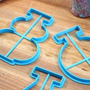 May include: Four blue plastic cookie cutters shaped like a snowman, a circle with a cross inside, and two other shapes. The cutters are on a wooden surface.