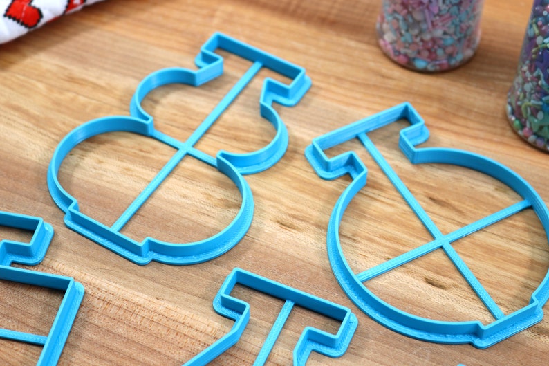 May include: Four blue plastic cookie cutters shaped like a snowman, a circle with a cross inside, and two other shapes. The cutters are on a wooden surface.