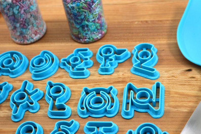 May include: A set of 15 blue plastic cookie cutters in various shapes, including circles, swirls, and geometric designs. The cutters are arranged on a wooden surface.