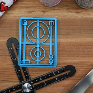 May include: A blue plastic cookie cutter shaped like a soccer field with a circle in the center and two smaller circles on the side.