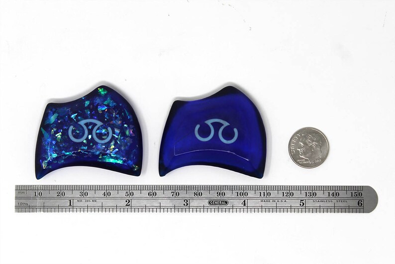 May include: Two blue glass decorative pieces with a white symbol in the center. The piece on the left has a glittery finish. The piece on the right is solid blue.