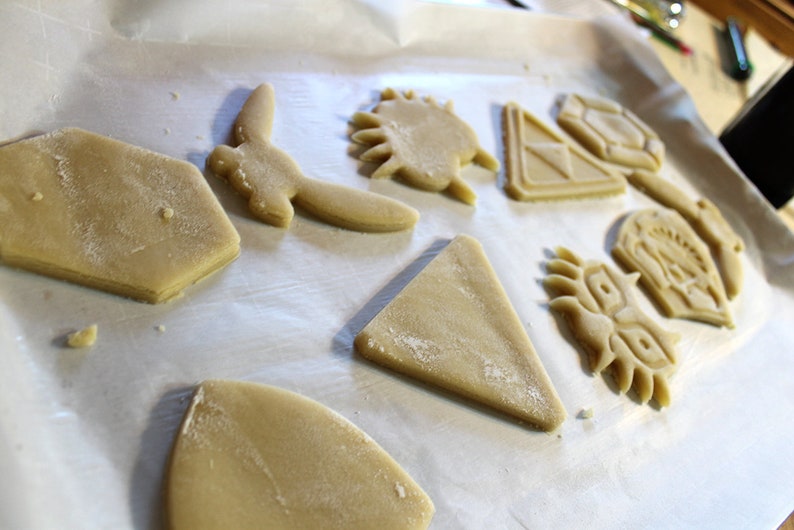 Puede incluir: Una hoja de papel para hornear con varias formas de masa para galletas sin hornear, incluyendo un tri&aacute;ngulo, un c&iacute;rculo, una estrella y algunas otras formas abstractas.