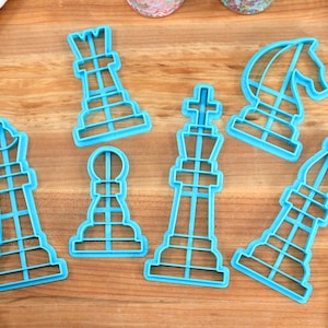 May include: A set of seven blue plastic cookie cutters shaped like chess pieces. The pieces include a king, queen, bishop, knight, rook, and two pawns.