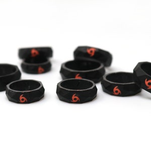 May include: A set of eight black silicone rings with a red swirl design. The rings are textured and have a geometric shape.