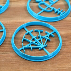May include: A set of four blue plastic cookie cutters with different designs. The cutters are on a wooden surface.