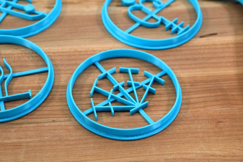 May include: A set of four blue plastic cookie cutters with different designs. The cutters are on a wooden surface.