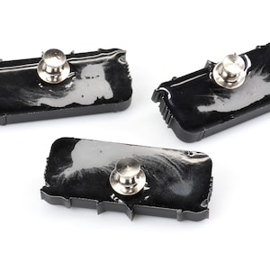 May include: Three black resin pins shaped like the outline of the United States. Each pin has a silver metal pin back.