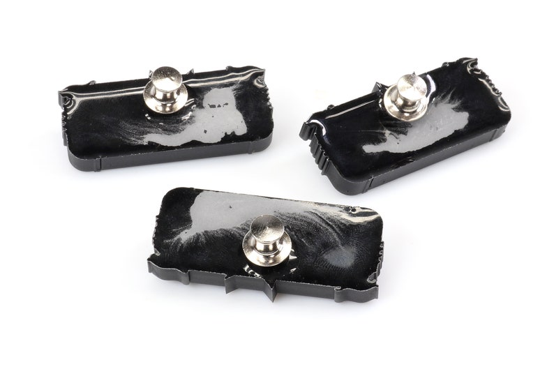 May include: Three black resin pins shaped like the outline of the United States. Each pin has a silver metal pin back.