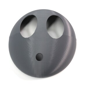May include: A gray plastic face mask with two large eye holes and a smaller hole in the center. The mask is designed to resemble a face.