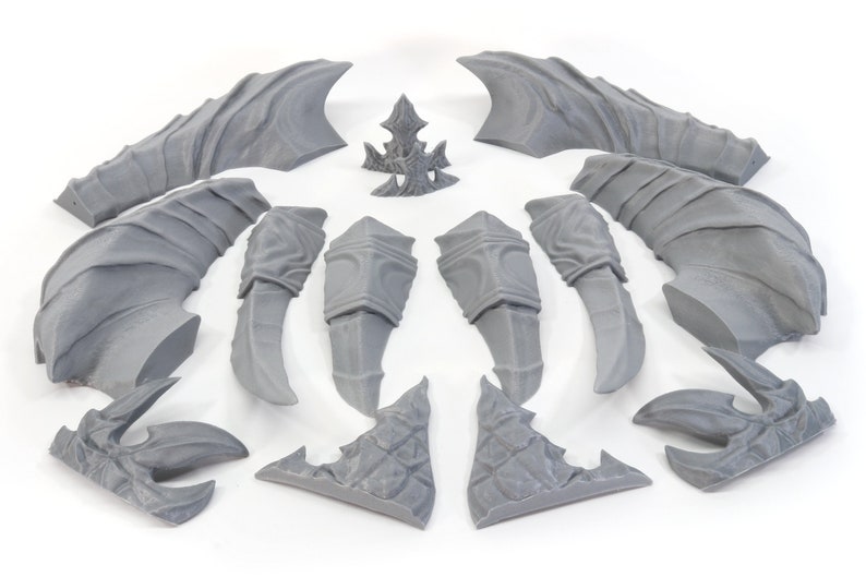 Pode incluir: Um conjunto de 14 pe&ccedil;as de pl&aacute;stico cinzento para um kit de modelo 3D. As pe&ccedil;as t&ecirc;m a forma de asas, garras e outras partes de uma criatura.