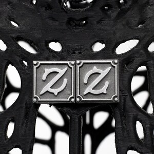 Op de afbeelding: Twee zilveren metalen vierkanten met de letter "Z" in een gestileerd lettertype op een zwarte achtergrond.