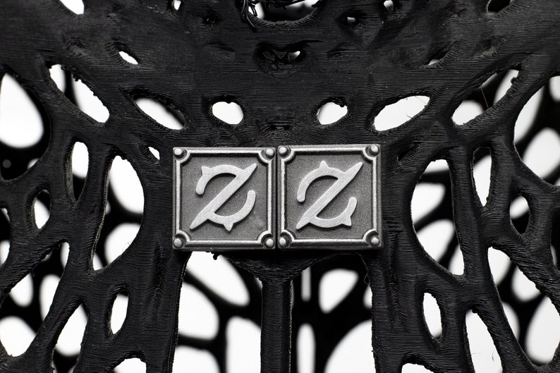 Op de afbeelding: Twee zilveren metalen vierkanten met de letter "Z" in een gestileerd lettertype op een zwarte achtergrond.