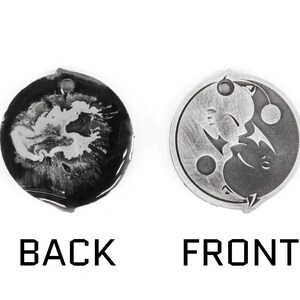 May include: A silver-colored metal charm with a yin yang design on one side and a blank surface on the other side.