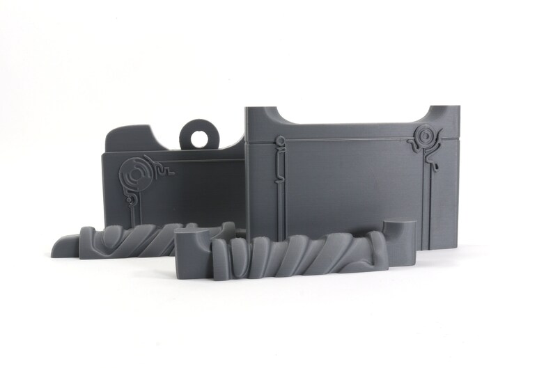 Może przedstawiać: Zestaw trzech szarych element&oacute;w wydrukowanych w 3D do miniaturowego modelu. Elementy to sekcja ściany z ozdobnymi detalami, sekcja ściany z okrągłym wzorem i zakrzywiony element z fakturowaną powierzchnią.