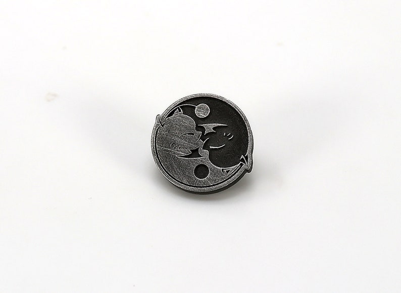 May include: A silver-toned yin yang pin with a cartoon dragon and a cartoon cat design.