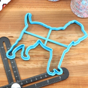 May include: A blue plastic cookie cutter shaped like a dog. The cutter is on a wooden surface with a ruler.