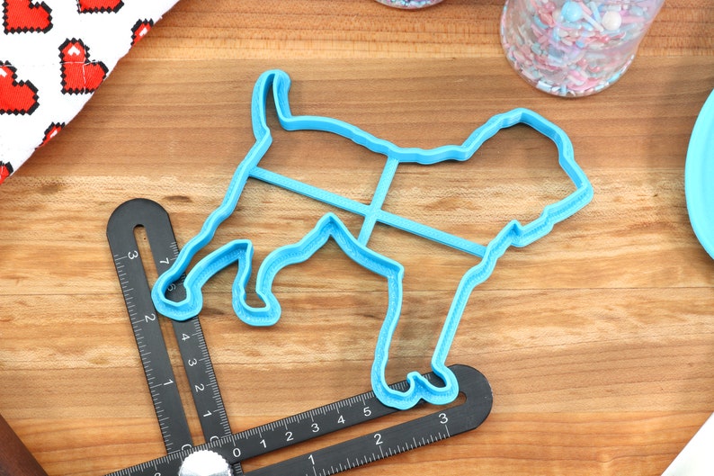 May include: A blue plastic cookie cutter shaped like a dog. The cutter is on a wooden surface with a ruler.