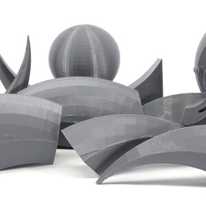 May include: A collection of gray 3D printed objects, including spheres, arches, and a more complex object with a star and three spheres. The objects are arranged on a white surface.